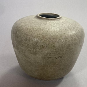 May include: A grey ceramic vase with a rounded body and a slightly flared opening. The vase has a textured surface.