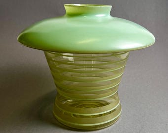 May include: A green glass vase with a wide, flat top and a cylindrical body. The body features horizontal stripes in a lighter shade of green. The vase has a unique, mushroom-like shape, and is likely a decorative item.