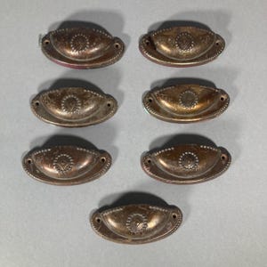May include: Eight antique brass cabinet knobs with a decorative design. The knobs are oval shaped with a raised centre and a beaded edge.