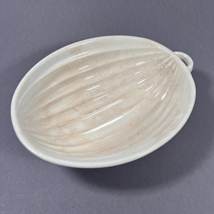 Puede incluir: Plato ovalado de cerámica blanquecina con asa. El interior presenta un diseño texturizado y acanalado con sombreado marrón. El plato tiene un acabado brillante. Aproximadamente 20 cm de largo, ideal para servir o exhibir.