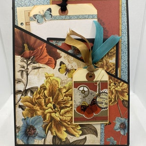 Op de afbeelding: Een scrapbook met een bloemenontwerp en een tag met een vlinder en de tekst "Maison Vendale Le Meilleur Mar 1946".