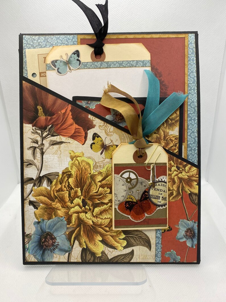 Op de afbeelding: Een scrapbook met een bloemenontwerp en een tag met een vlinder en de tekst "Maison Vendale Le Meilleur Mar 1946".