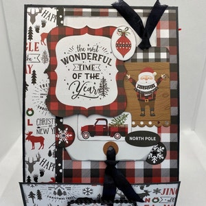 May include: A Christmas-themed scrapbook page with a red and black plaid pattern. It features decorative elements like a Santa Claus illustration, a red truck carrying a Christmas tree, and the text "the most wonderful time of the year."