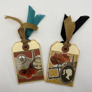 Op de afbeelding: Twee decoratieve labels met een bruin lint en een bruine papieren achtergrond. Een label heeft een vlinder, tandwielen en de tekst "Maison Vendale Le Meilleur March&eacute; de". Het andere label heeft een rode bloem, een filmstrip en een silhouet van een vrouw.