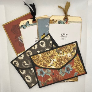 Op de afbeelding: Vier decoratieve enveloppen met bloemen- en silhouetpatronen. Elke envelop heeft een zwarte rand en een flap met een zak. De enveloppen liggen op elkaar. De bovenste envelop heeft een bloemenpatroon met vlinders en de tekst "Place Photo Here" en "Photographs & Memories".