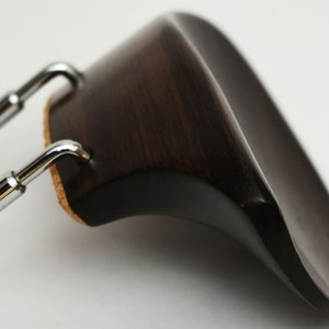 May include: A dark brown wooden violin shoulder rest with a chrome metal adjustable strap.