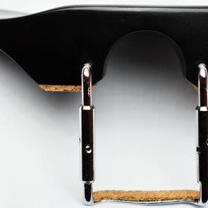 May include: A black violin shoulder rest with a curved design. It features a wooden frame with a cork pad and adjustable metal brackets. The shoulder rest is designed to provide comfort and support for violin players.