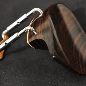 May include: A dark brown wooden violin shoulder rest with a silver metal adjustment mechanism. The shoulder rest has a curved shape and a smooth finish.