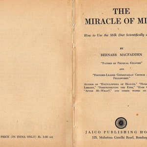 May include: An open vintage book titled "THE MIRACLE OF MILK" with text about using the milk diet. The cover is tan with black text. The author is Bernarr Macfadden. Published by Jaico Publishing House.