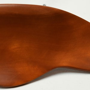 May include: A wooden, brown, ergonomic desk accessory with a curved design. The accessory is a warm, medium brown colour and has a smooth, polished finish. Two small metal hooks are attached to the top.