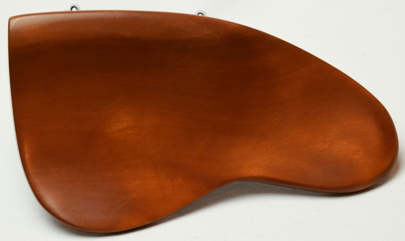 May include: A wooden, brown, ergonomic desk accessory with a curved design. The accessory is a warm, medium brown colour and has a smooth, polished finish. Two small metal hooks are attached to the top.