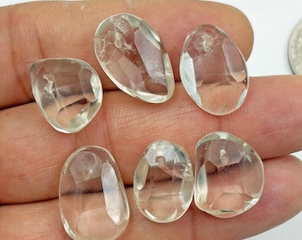 Puede incluir: Seis cuentas de cuarzo transparente, facetadas y de forma irregular. Cada cuenta presenta una superficie lisa y pulida con inclusiones naturales internas y un orificio perforado cerca del borde superior, mostrando un aspecto transparente y vítreo.