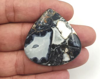 May include: A teardrop-shaped polished gemstone featuring a high-contrast pattern of solid black, creamy white, and dark gray sections. The surface is smooth and reflective, showcasing distinct organic shapes and veins throughout the stone.