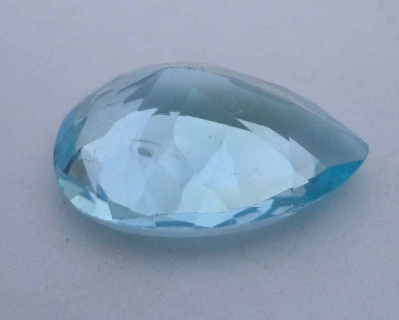 May include: A light blue pear-shaped gemstone with a faceted cut.