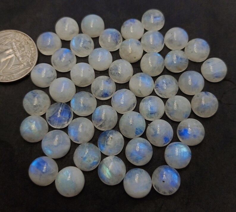 Op de afbeelding: Een verzameling van 35 ronde, witte maansteen cabochons met iriserende blauwe en groene schittering. De cabochons zijn ongeveer 10 mm in diameter.