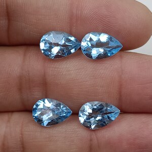 May include: Four pear-shaped, light blue topaz gemstones. The gemstones are faceted and have a brilliant shine.