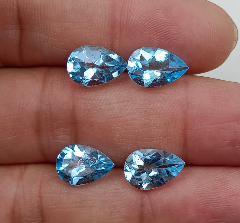 May include: Four pear-shaped, light blue topaz gemstones. The gemstones are faceted and have a brilliant shine.