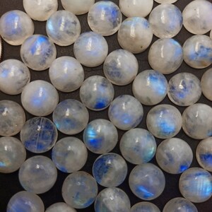 Op de afbeelding: Een verzameling ronde, iriserende maansteen cabochons. De stenen zijn melkachtig wit met een blauwe schijn.