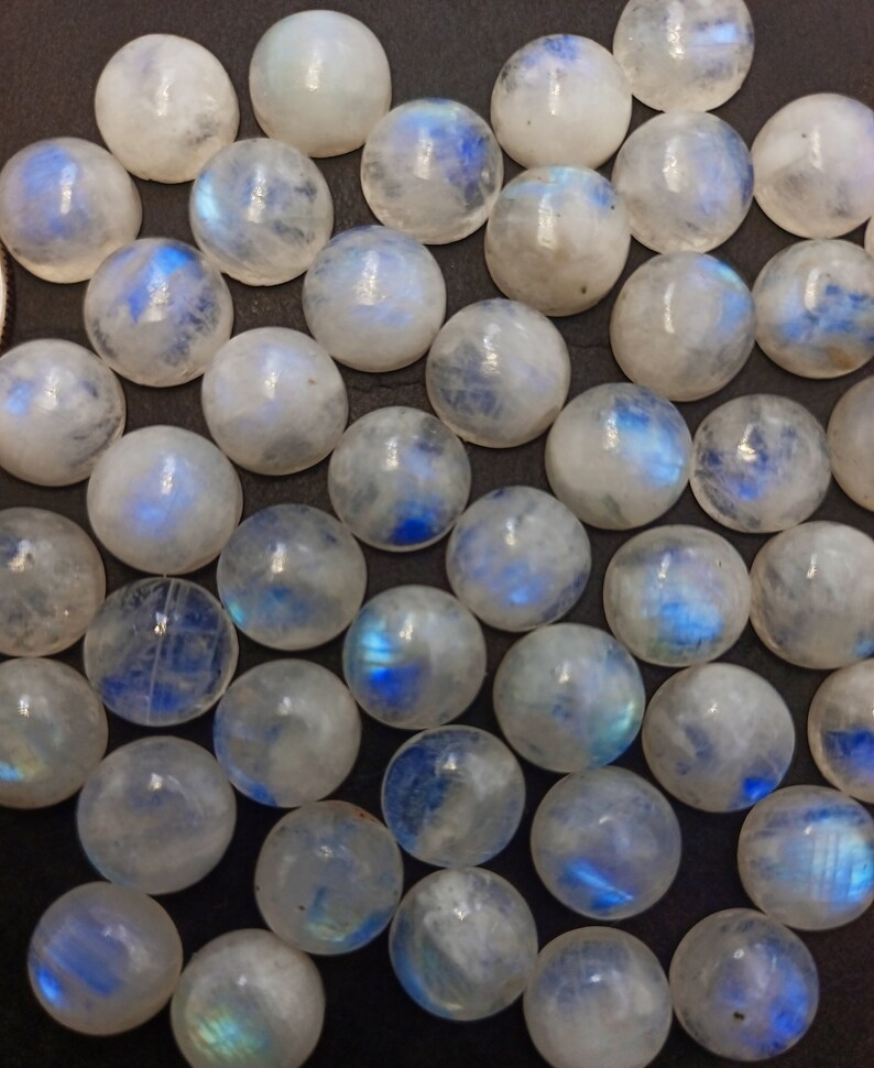 Op de afbeelding: Een verzameling ronde, iriserende maansteen cabochons. De stenen zijn melkachtig wit met een blauwe schijn.