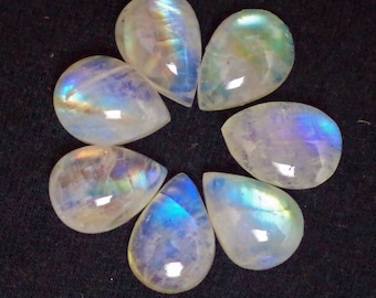 Op de afbeelding: Zeven regenboogkleurige, parelmoerachtige, druppelvormige maansteen-cabochons in verschillende tinten wit, blauw en groen.