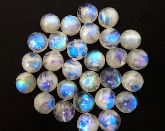 Op de afbeelding: Een verzameling van 25 ronde, iriserende maansteen cabochons. De stenen zijn melkachtig wit met een blauwe en groene adularescence.