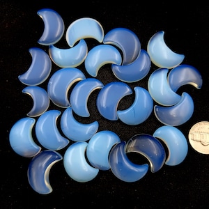 May include: A collection of 20 blue and white crescent moon shaped cabochons. The cabochons are made of opal and have a smooth, polished finish.
