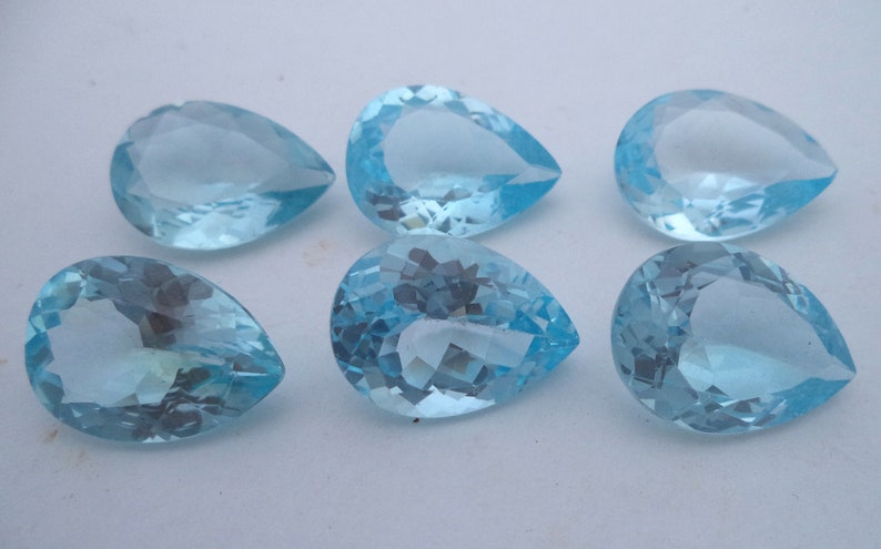 May include: Six pear-shaped, light blue gemstones. The gemstones are faceted and have a clear, glassy appearance.