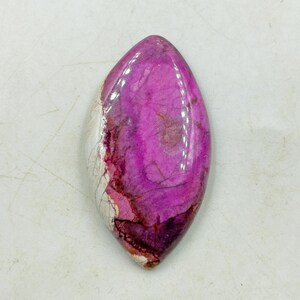 Pu&ograve; includere: Una gemma lucida e allungata con una vibrante tonalit&agrave; magenta, venata di tonalit&agrave; pi&ugrave; scure di rosso e viola. La pietra ha una superficie liscia e lucida e una sezione di marmorizzazione bianca e crema. La forma generale ricorda una lacrima o un occhio.
