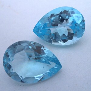 May include: Two teardrop-shaped, faceted, light blue gemstones. The gemstones are clear and have a slight sparkle.