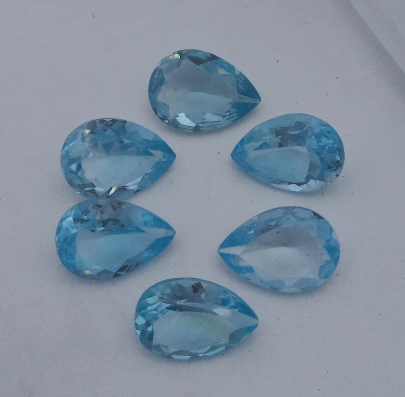 May include: Six pear-shaped, light blue gemstones. The gemstones are faceted and have a smooth, polished finish.