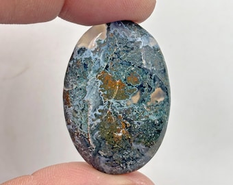May include: A green, brown, and white agate cabochon with a unique, swirling pattern. The cabochon is oval shaped and has a smooth, polished surface.