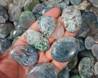 May include: A hand holding a variety of green and white agate stones. The stones are smooth and polished, and they have a variety of patterns and shapes.