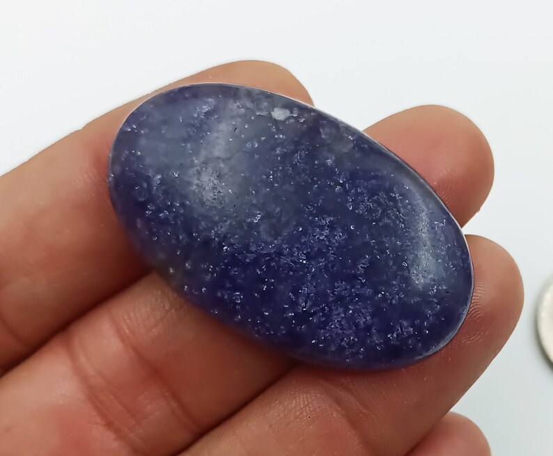K&ouml;nnte beinhalten: Ein glatter, ovaler blauer Edelstein mit einer funkelnden, strukturierten Oberfl&auml;che. Der Stein hat eine hellblaue Farbe mit dunkleren blauen Flecken.