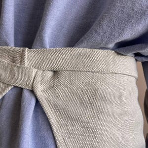 May include: A light blue shirt with a beige fabric belt tied around the waist.
