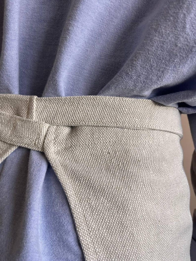 May include: A light blue shirt with a beige fabric belt tied around the waist.