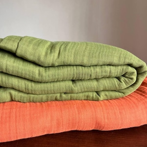 May include: Folded green and orange fabric. The green fabric is folded on top of the orange fabric. The fabrics appear to be made of a soft, textured material. The image is a close-up shot of the folded fabrics.