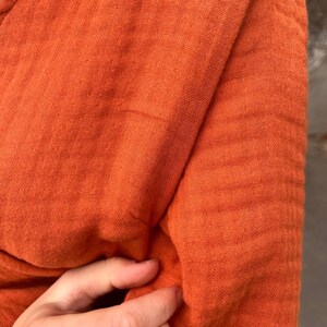 May include: Close-up of a textured, orange fabric. The fabric is folded, revealing the weave and texture. The color is a vibrant, warm orange, suggesting a garment or textile.