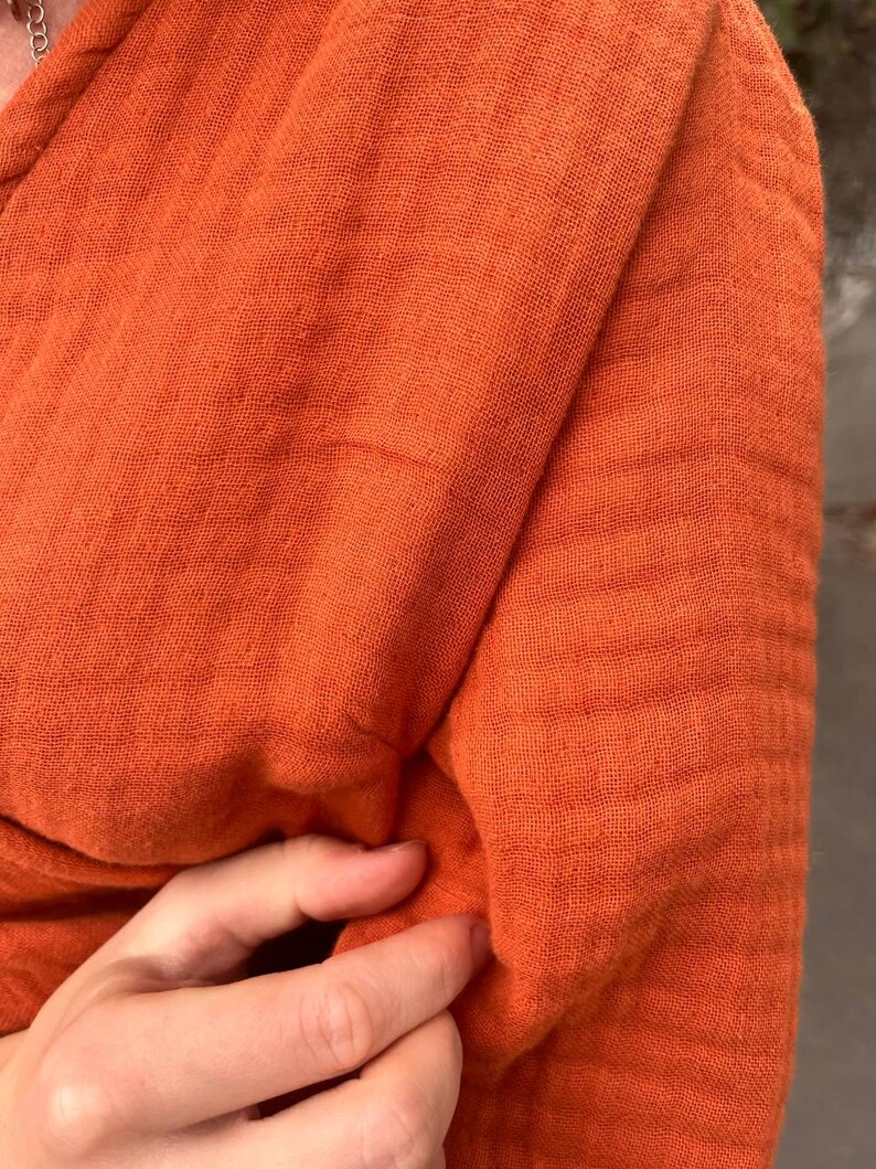 May include: Close-up of a textured, orange fabric. The fabric is folded, revealing the weave and texture. The color is a vibrant, warm orange, suggesting a garment or textile.
