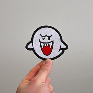Puede incluir: Un fantasma blanco con un contorno negro y ojos y dientes rojos. El fantasma sonr&iacute;e con una amplia sonrisa de dientes.