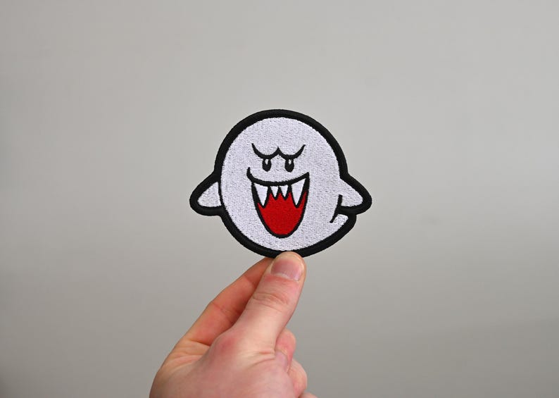 Puede incluir: Un fantasma blanco con un contorno negro y ojos y dientes rojos. El fantasma sonr&iacute;e con una amplia sonrisa de dientes.
