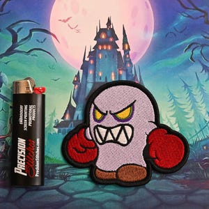 May include: Embroidered patch of an angry cartoon ghost with red boxing gloves and brown feet. A black lighter with "Precision Stitches" text is next to the patch. The background shows a spooky castle and a full moon.