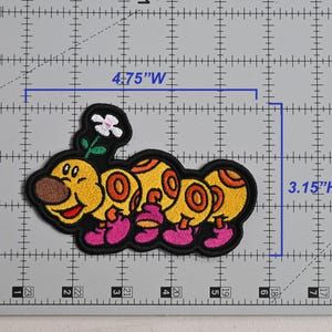 May include: Embroidered patch featuring a cartoon caterpillar with a flower. The caterpillar is yellow with orange and brown details, pink feet, and a black outline. The patch measures 4.75 inches wide and 3.15 inches high.