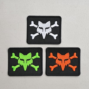May include: Three square patches with a fox skull and crossbones design. One patch has a white fox skull and crossbones on a black background. The other two patches have a green and orange fox skull and crossbones on a black background.