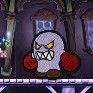 May include: Embroidered patch of an angry cartoon ghost with yellow eyes and red boxing gloves. The ghost is light purple with a black outline. The background shows a video game scene with a character and a spooky castle.