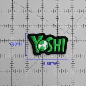 May include: Embroidered patch featuring the word "YOSHI" in bright green, outlined in black. The patch is 2.65 inches wide and 1.50 inches high. The "O" in "YOSHI" features a white and green design. The patch is likely for clothing or accessories.