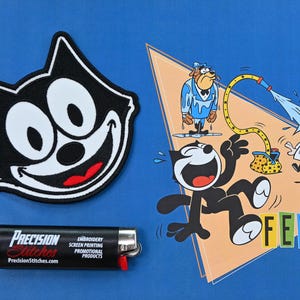 May include: A black and white Felix the Cat patch and a cartoon illustration of Felix the Cat being sprayed with water. A black lighter with the text "Precision Stitches" is also in the image.