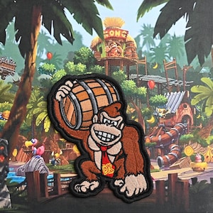 May include: Embroidered patch featuring Donkey Kong carrying a barrel. The patch is brown, black, and white with a red tie and the letters "DK" on the tie. The background is a cartoon jungle scene.