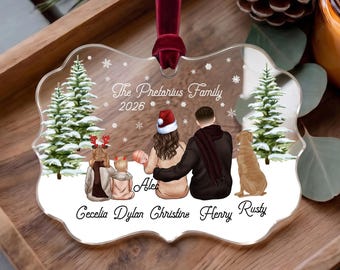 May include: A clear, scalloped-edge acrylic ornament hanging from a dark red velvet ribbon. The design features a family illustration with two snow-covered pine trees, snowflakes, and the text: The Pretarius Family 2026, Alec, Cecelia, Dylan, Christine, Henry, Rusty.