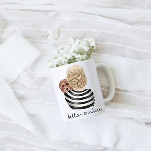 May include: White ceramic mug with a black and white illustration of a woman with a dog on her shoulder. The text "bella ♥ alice" is printed on the mug.