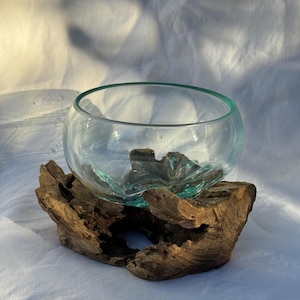 Peut inclure: Un bol en verre transparent avec un bord turquoise est posé sur un morceau de bois flotté vieilli. Le bol est de forme arrondie et vide. La base en bois flotté présente une texture naturelle et organique. Le fond est en tissu blanc.